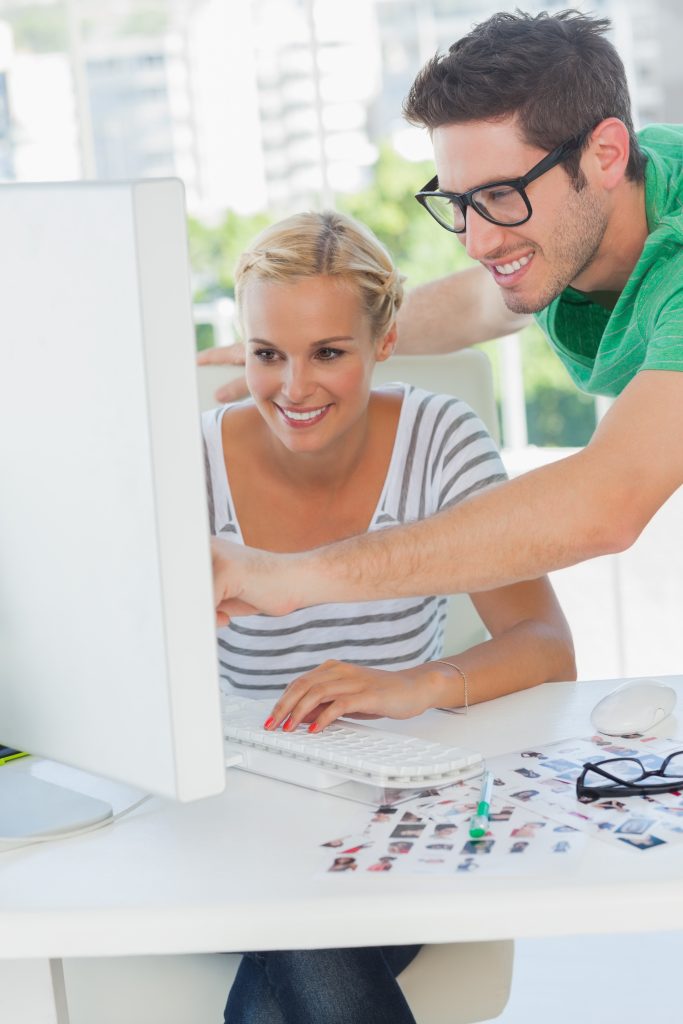 Cheerful photo editor pointing at a computer with a colleague